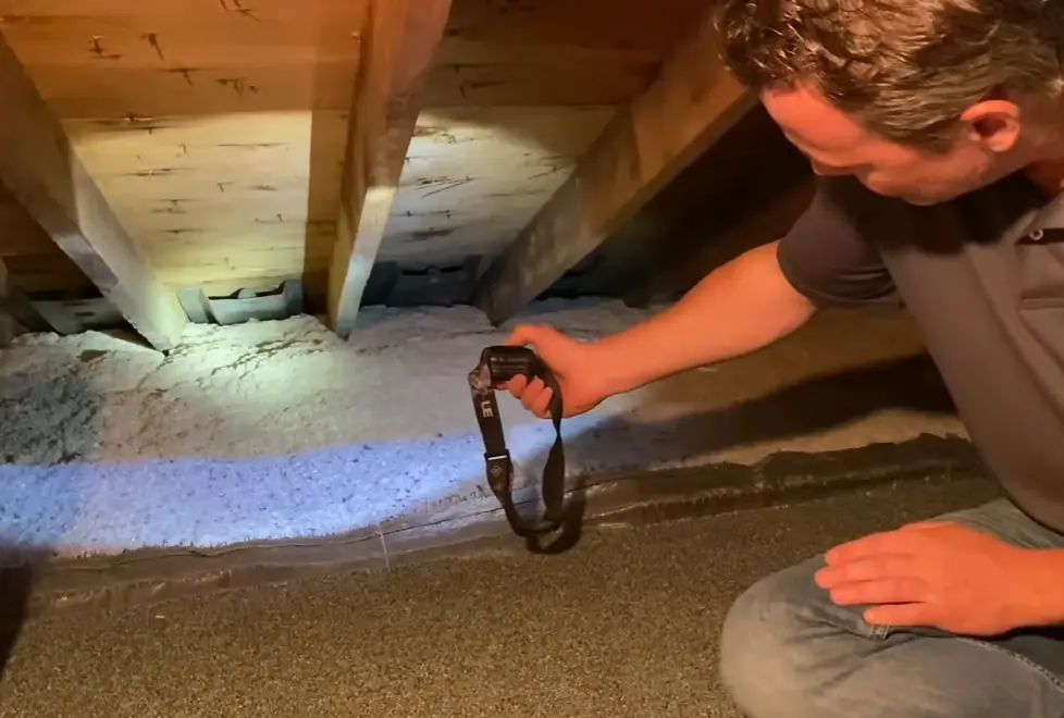 A roofing professional inspecting attic baffles with a flashlight to ensure proper airflow for roof ventilation