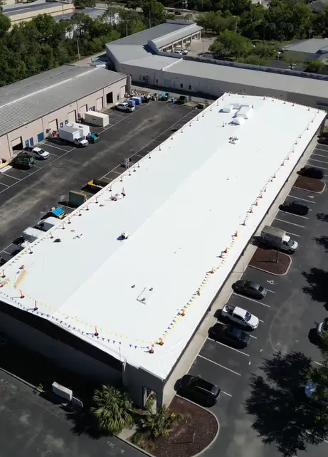 Aerial view of a bright white, completed commercial flat roof surrounded by perimeter safety flags.