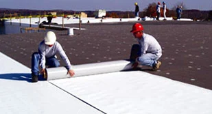 Professional roofers unrolling white TPO membrane on flat roof.