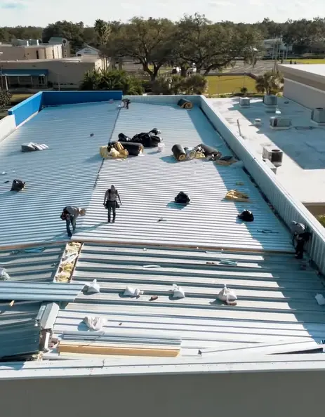 Professional roofing crew actively installing large metal roof panels on a commercial building deck.