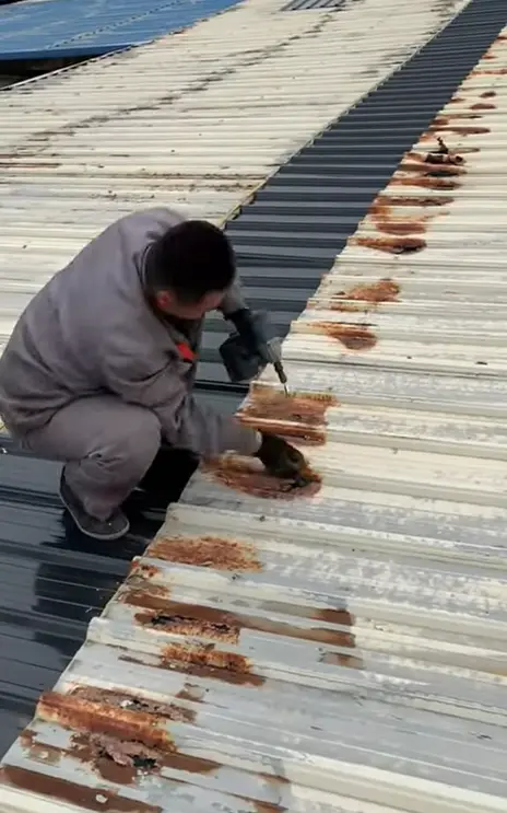 Worker using power tools to repair rusted corrugated metal roofing on a commercial building