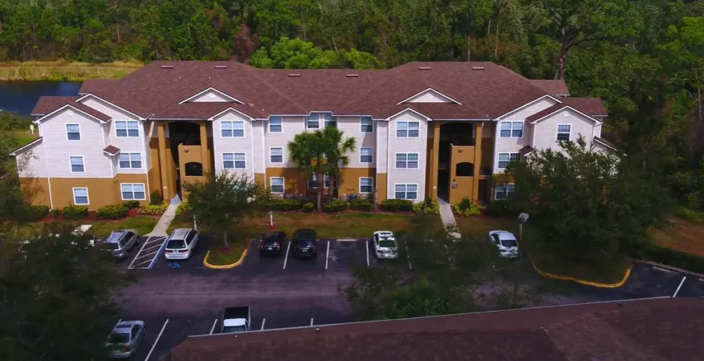 Aerial overhead view of a large apartment complex featuring a brown asphalt shingle roof.