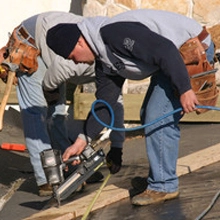 Roofers installing asphalt shingles with nail gun during residential roof replacement in Gainesville FL
