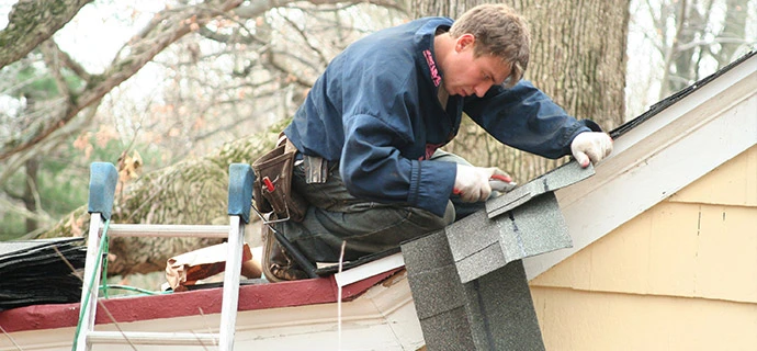 Professional roofer replacing damaged shingles on a residential roof near a fallen tree limb