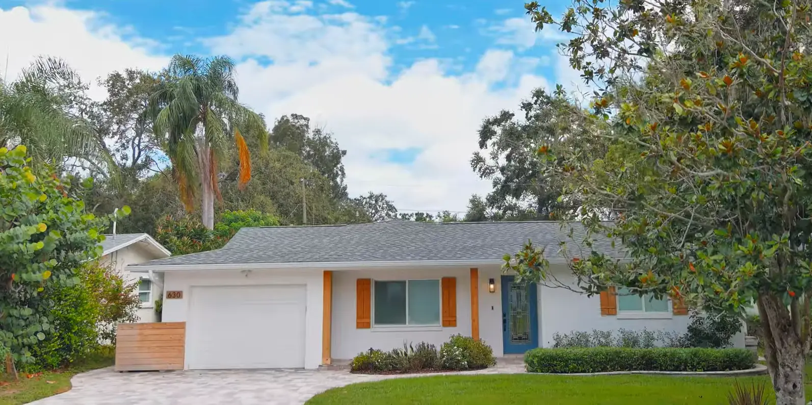 White ranch-style home with a grey shingle roof surrounded by oak trees
