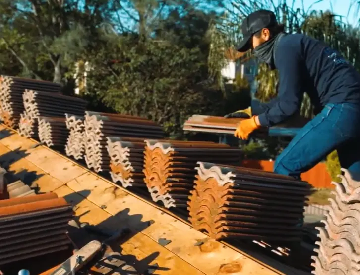 A roofer carefully stacks terracotta clay tiles on a wooden roof deck.