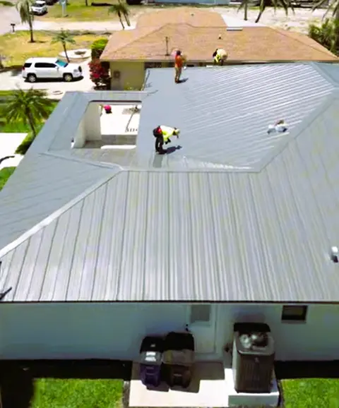 Roofing crew safely installs a light grey standing seam metal roof on a house.