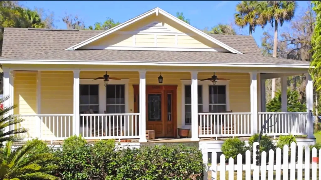 A yellow Florida home featuring a clean asphalt shingle roof over a large porch.